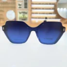 Gros plan sur des lunettes clips oversize bleu vibrant, monture angulaire brillante avec détails carrés sur les branches.