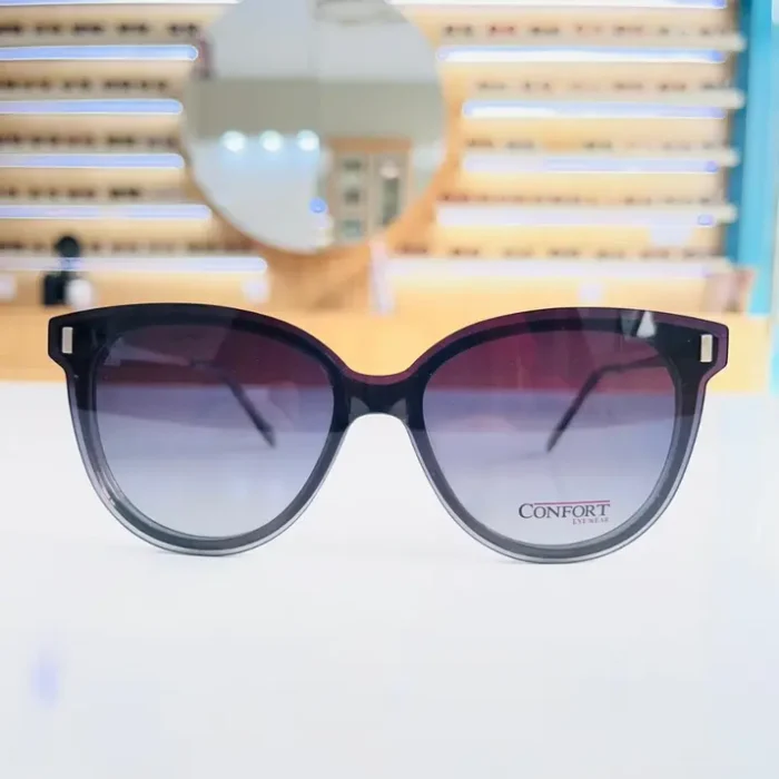 Gros plan de lunettes œil de chat noires avec dégradé gris, monture épaisse, branches larges et détails métal aux coins.