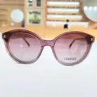 Gros plan sur lunettes œil de chat rose transparent, branches fines et décor carré aux coins supérieurs.