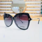 Présentation de lunettes de soleil oversize noires à monture épaisse, avec branches en métal doré texturé, montrées sous plusieurs angles.