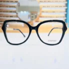 Gros plan sur les branches de lunettes de soleil oversize noires, finition brillante, avec détail tressé sur une branche fine.