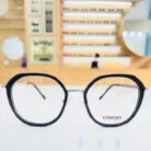 Lunettes hexagonales noires fines avec pont transparent et branches légères, style moderne et élégant.