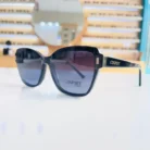 Lunettes œil de chat noires en plastique brillant portées en extérieur, branches larges avec logo visible.