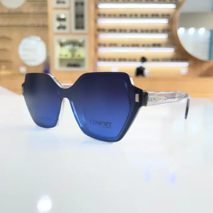 Lunettes oversize bleues portées, monture angulaire avec branches transparentes et détails visibles pour un look moderne.