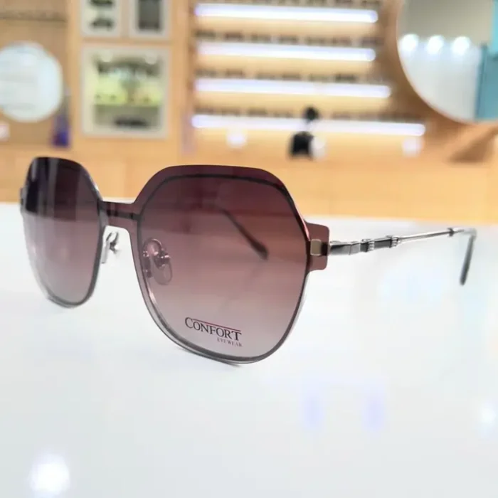 Gros plan de lunettes oversize marron, forme géométrique, branches fines argentées avec détails métallisés, look chic.