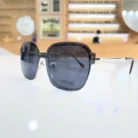 Lunettes oversize noires portées en extérieur, forme carrée avec branches en métal et embouts noirs, style élégant.