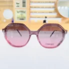 Lunettes oversize roses en plastique brillant portées en extérieur, monture large avec branches fines translucides.