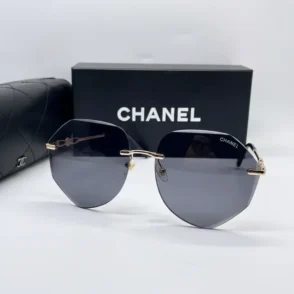 Chanel lunette de soleil femme à monture métal fine et branches dorées, verres teintés foncés, étui noir en arrière-plan.