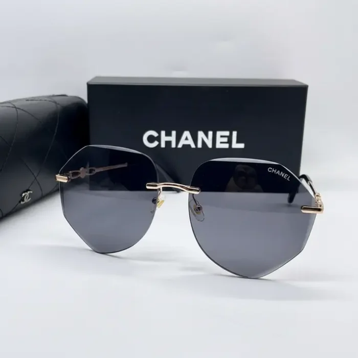 Chanel lunette de soleil femme à monture métal fine et branches dorées, verres teintés foncés, étui noir en arrière-plan.