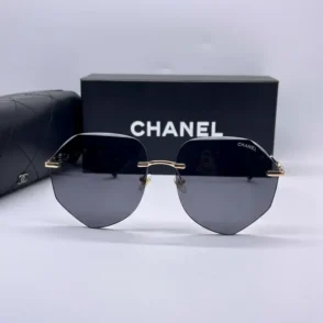 Chanel lunettes de soleil à verres octogonaux teintés, sans monture, avec branches fines dorées et boîte CHANEL en arrière-plan.