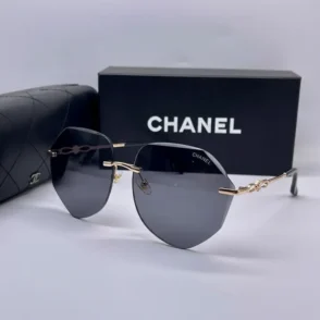 Lunette de soleil Chanel avec monture métallique dorée fine et verres gris foncé, posée près d’un étui et d’une boîte Chanel.