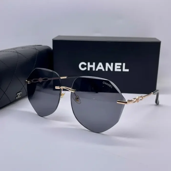 Lunette de soleil Chanel avec monture métallique dorée fine et verres gris foncé, posée près d’un étui et d’une boîte Chanel.