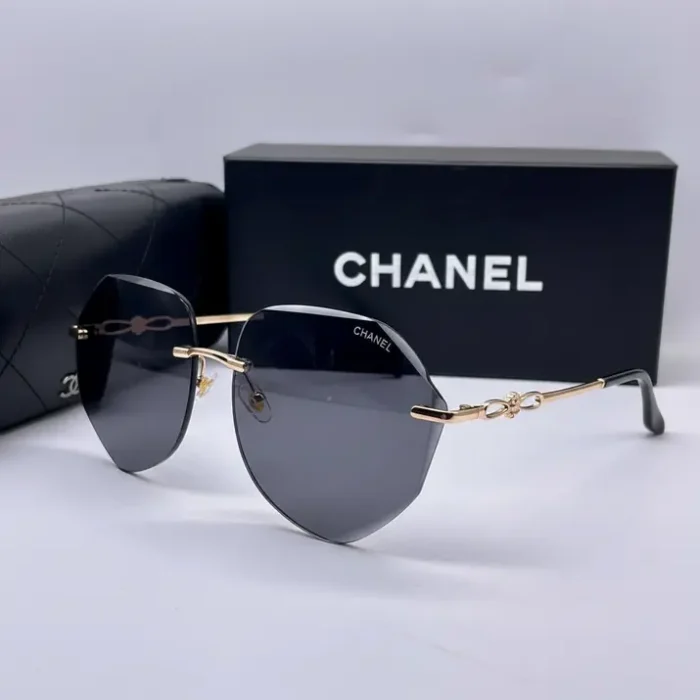 Lunette de soleil femme Chanel avec verres foncés géométriques, monture métal doré et étui Chanel en arrière-plan.