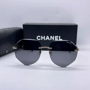 Lunette de soleil homme Chanel hexagonale avec verres noirs, branches dorées, posée devant une boîte CHANEL et un étui noir.