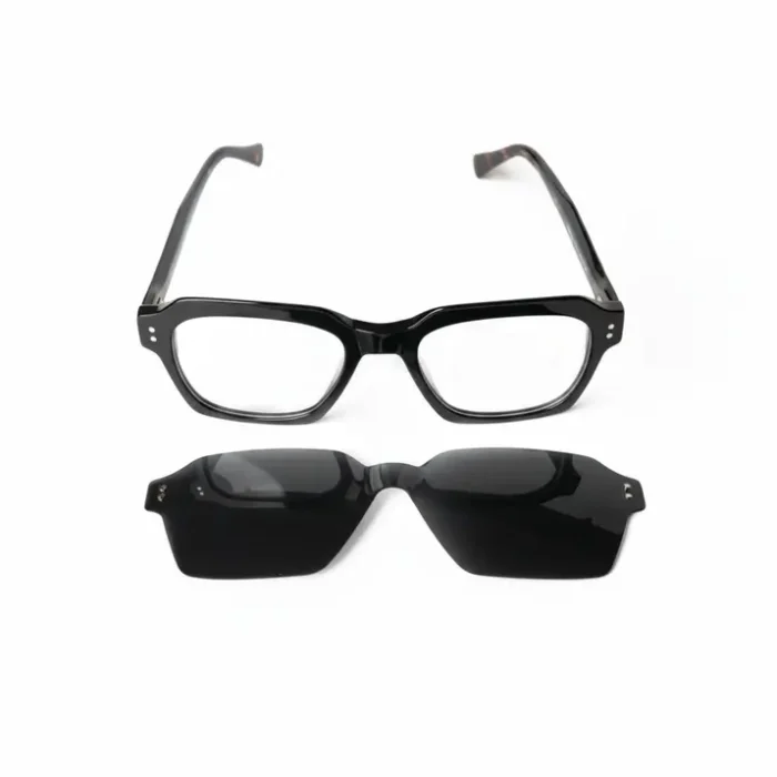Clip lunette soleil à verres teintés noirs placé sous une monture de lunettes noire, prêt à se fixer pour protection UV.