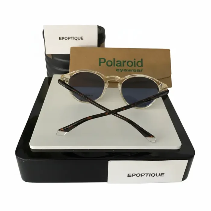 Lunette de soleil Polaroid rondes à monture transparente Lunette de soleil Polaroid avec verres ronds teintés, monture transparente et branches fines écaille, étui Polaroid en fond.